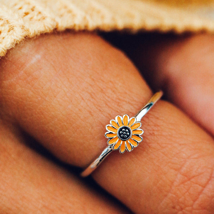 Close-up of sunflower ring worn on a finger with orange petals and a dark center