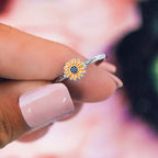 Enamel sunflower ring on finger featuring orange petals and a dark center on a slim silver band