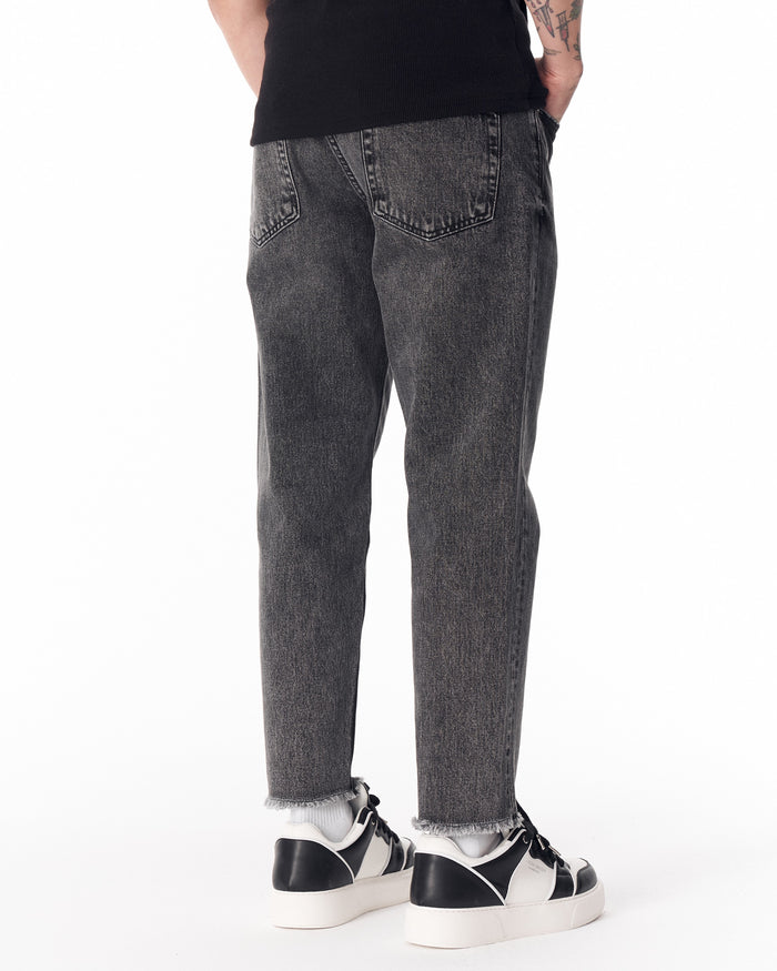 Martin Valen men's faded black jeans, low shot showing raw frayed hem and black-and-white sneakers
