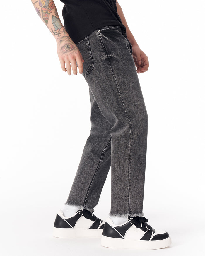 Martin Valen men's faded black jeans, side view showing straight leg and raw hem near ankle