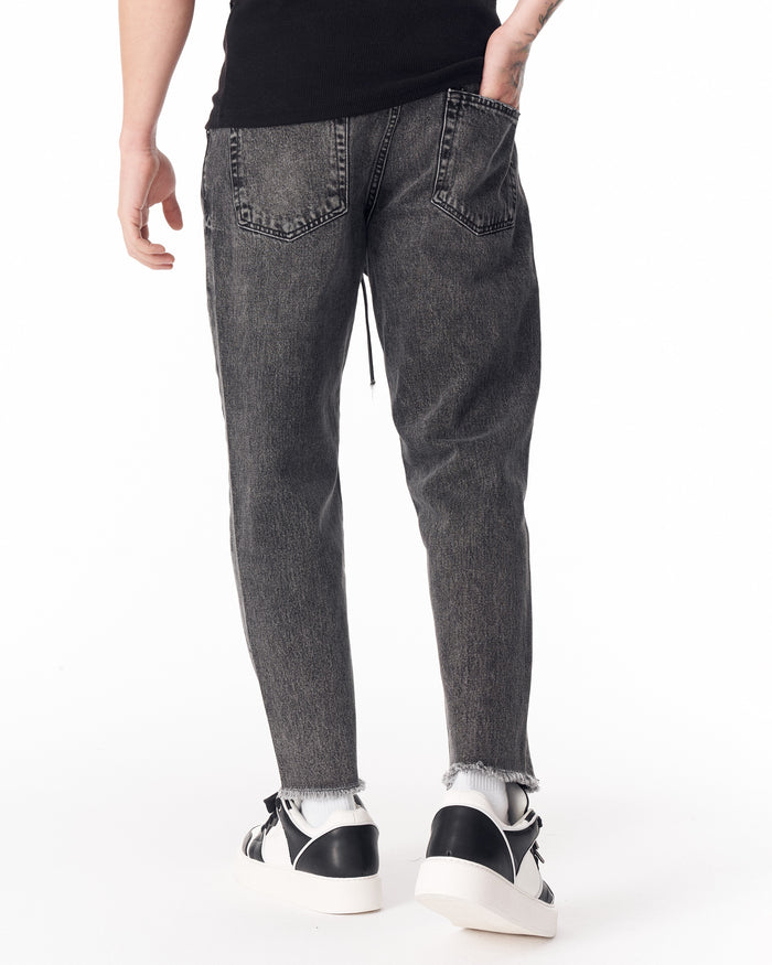 Martin Valen men's faded black jeans, close-up at ankle revealing raw frayed hem and black‑white sneakers