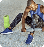Man using a recovery tool on his calf outdoors next to a green foam roller, demonstrating the RAD Muscle Flushing Kit | RAD for muscle recovery and wellness.