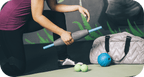 Person using the RAD Muscle Flushing Kit | RAD on their leg while kneeling on a yoga mat, with massage balls and a gym bag nearby, promoting muscle recovery and wellness.