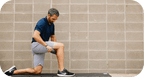 Man using RAD Muscle Flushing Kit | RAD for muscle recovery on thigh while kneeling on a mat against a gray brick wall, promoting wellness and body care.