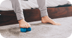 Person using feet to roll a small blue massage tool on carpet for muscle relief and recovery with RAD Roller Soft | RAD.
