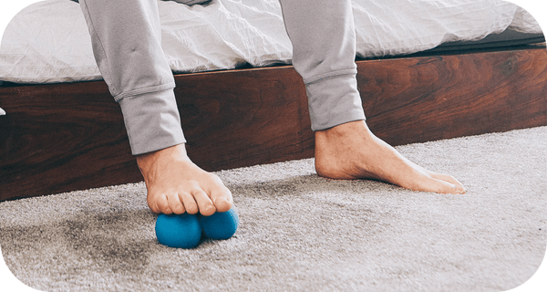 Person using feet to roll a small blue massage tool on carpet for muscle relief and recovery with RAD Roller Soft | RAD.