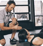 A man guides a woman using the RAD Roller Soft | RAD for targeted muscle recovery and body care, demonstrating its use on her upper back and neck in a wellness setting.