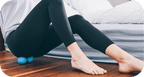 Person using a RAD Roller Soft | RAD for muscle recovery and body care on hardwood floor beside a bed, demonstrating wellness and relaxation at home.