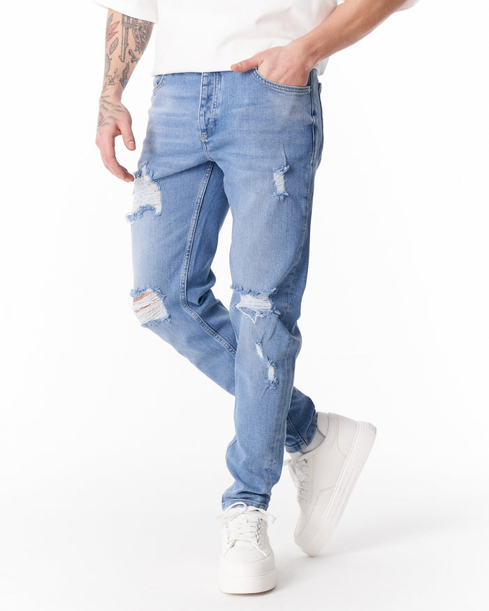 Martin Valen ripped slim-fit jeans in washed blue, lower-leg view showing frayed knees, hems and white sneakers