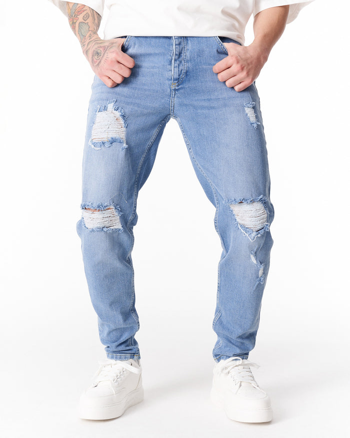 Martin Valen ripped slim-fit jeans in washed blue, mid-leg view with hands in pockets and knee distressing