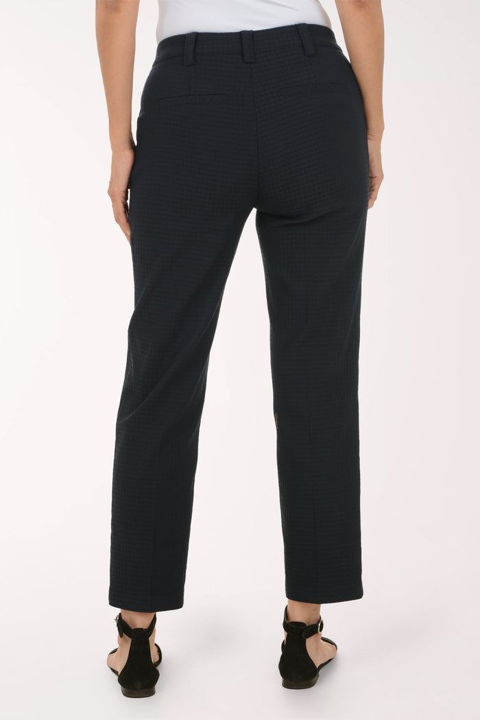 A person shown from the back wearing dark charcoal cropped trousers with a subtle textured pattern, paired with black strappy sandals against a plain white studio background.