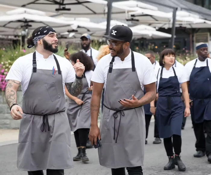 Group of people wearing aprons walking outdoors under umbrellas.